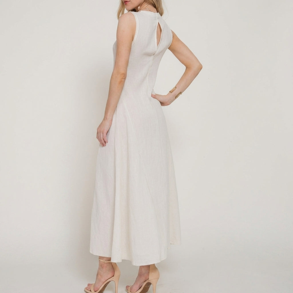 Woman in a sleeveless white dress with heels, poses against a plain background.