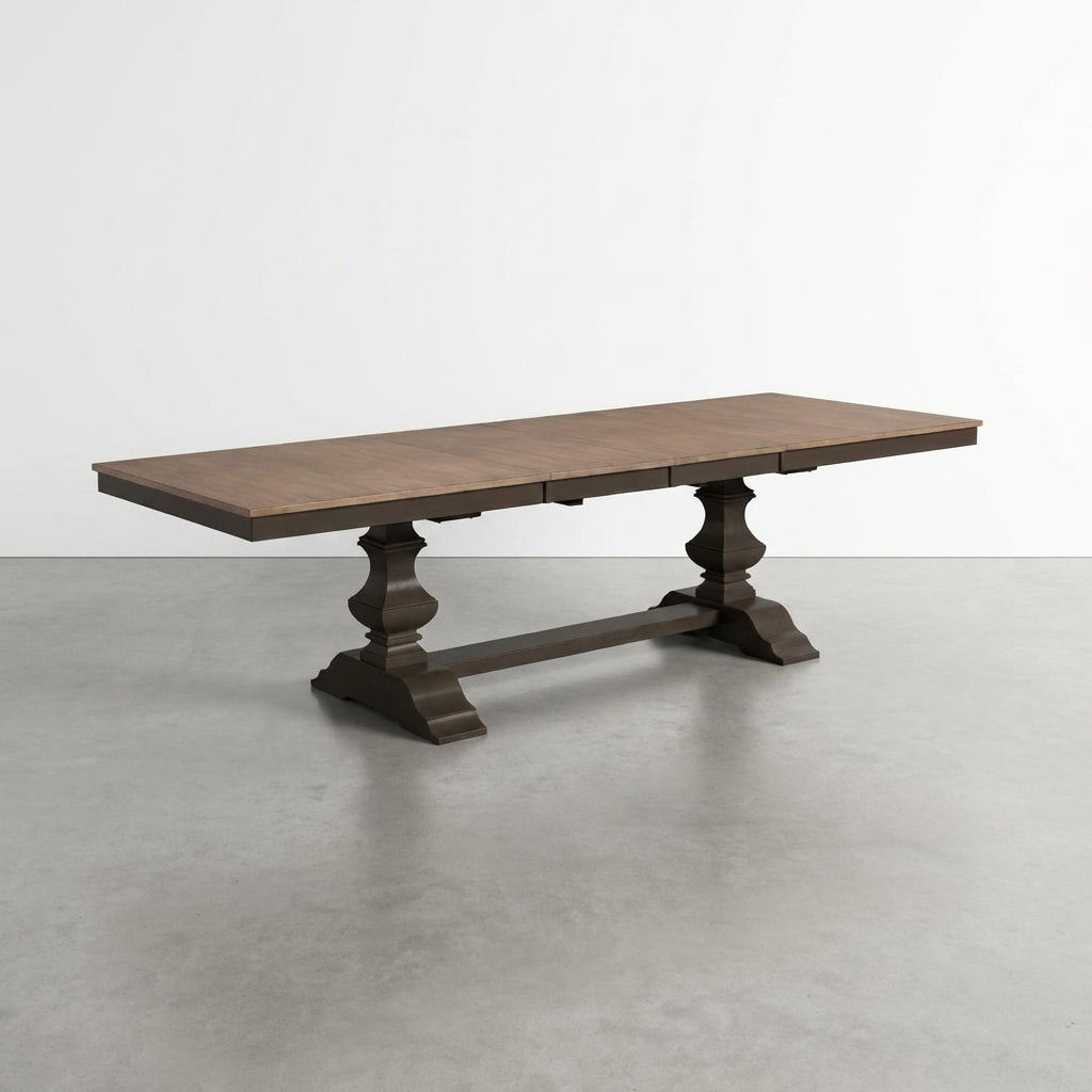 Wooden dining table with ornate pedestal legs on a gray floor.