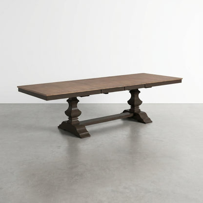 Wooden dining table with ornate pedestal legs on a gray floor.