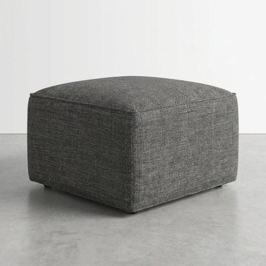Gray square ottoman on a concrete floor.