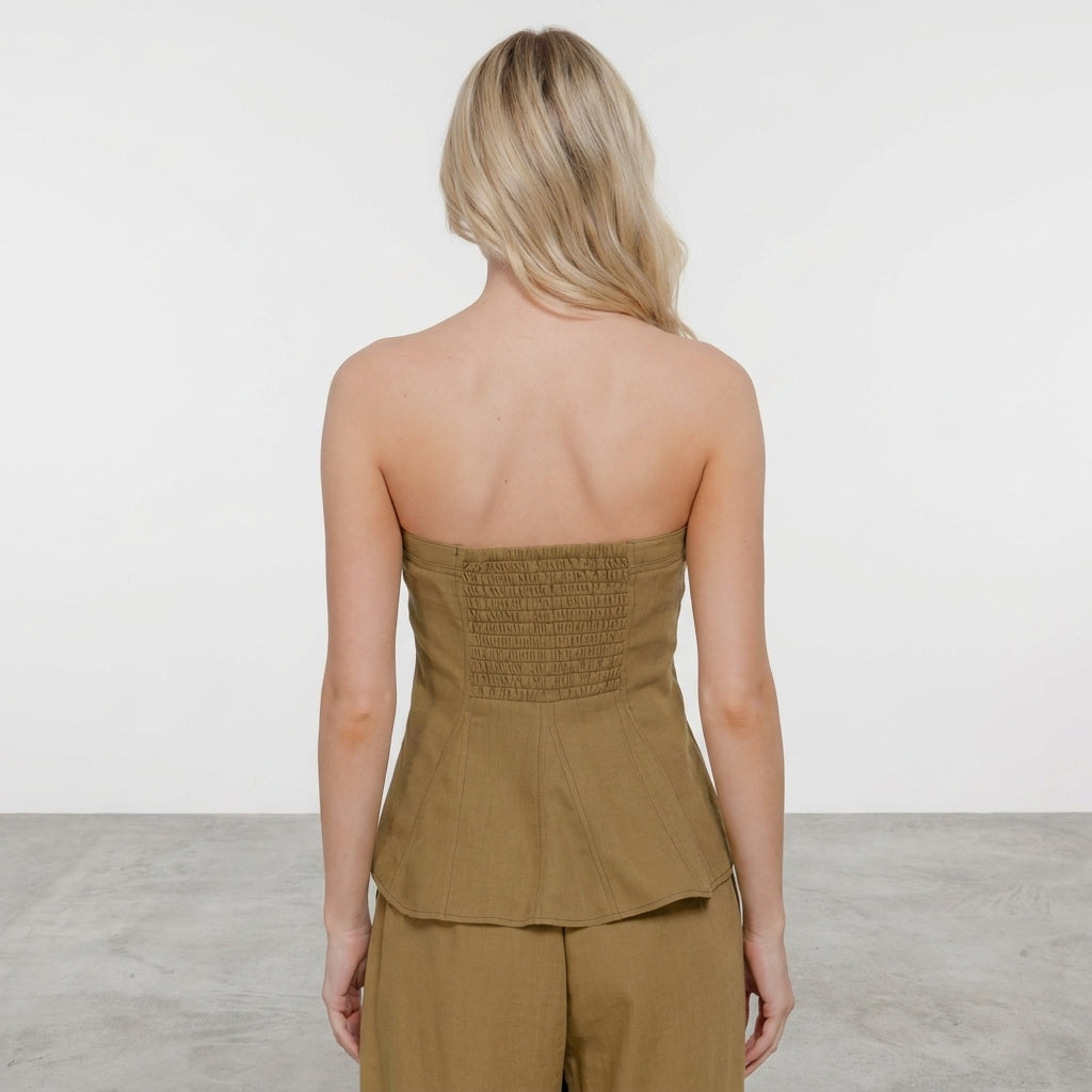 Woman in strapless olive outfit facing away in minimalist room.