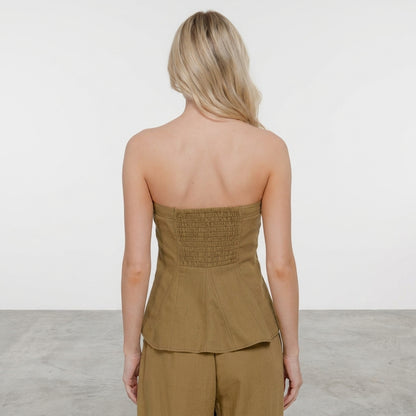 Woman in strapless olive outfit facing away in minimalist room.