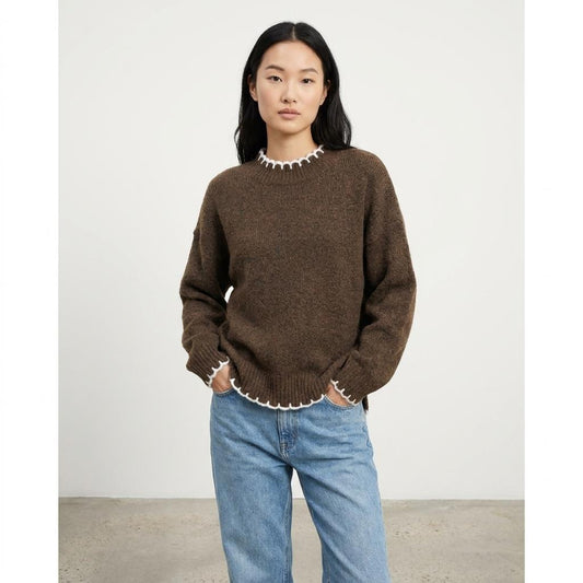 Person in a brown sweater and jeans, standing against a plain background.