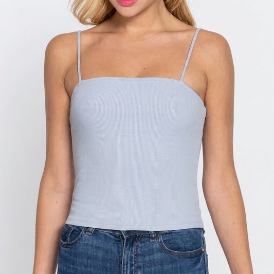Woman in light blue tank top and jeans against a plain background.