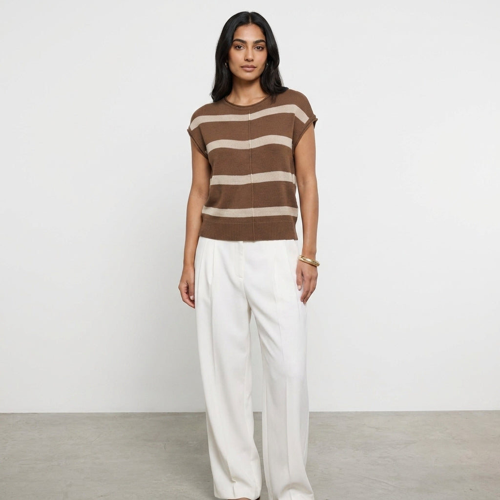 Person wearing a striped brown top and white pants, standing against a plain background.