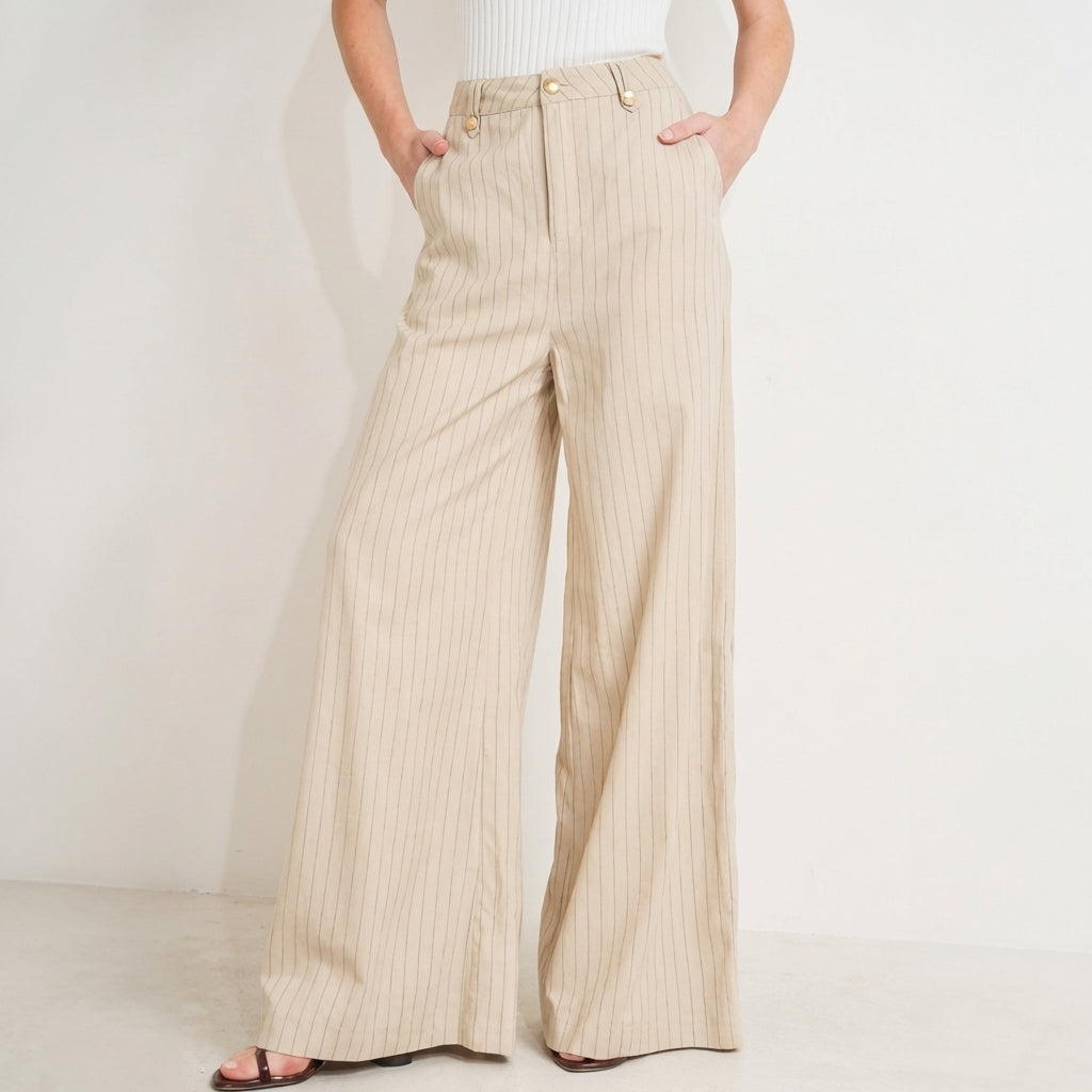 Wide-leg beige pants with pinstripes and hands in pockets.
