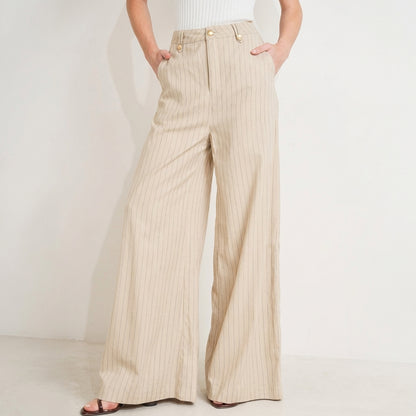Wide-leg beige pants with pinstripes and hands in pockets.