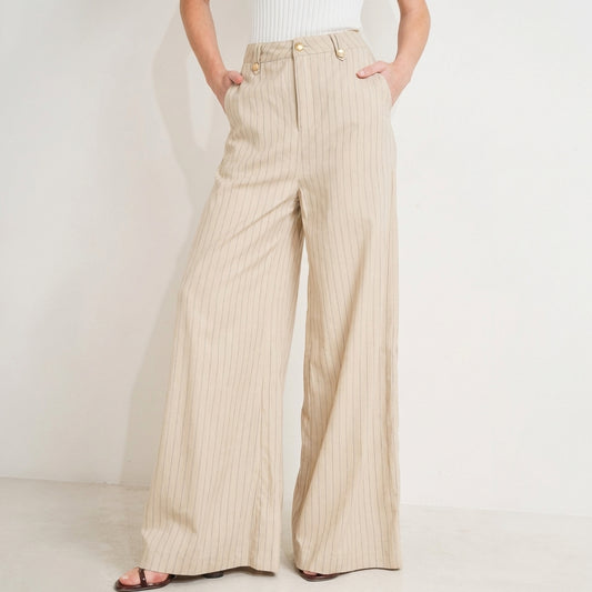 Wide-leg beige pants with pinstripes and hands in pockets.