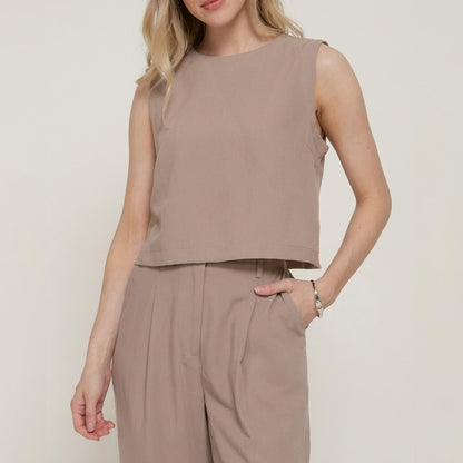 Woman in a sleeveless taupe outfit with hand in pocket.