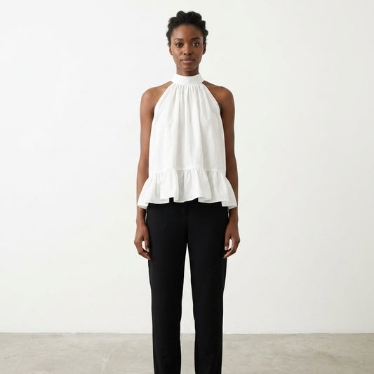 Person in white top and black pants stands against plain background.
