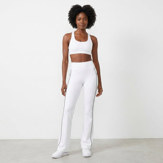 White flared pants with black piping, paired with striped sneakers.