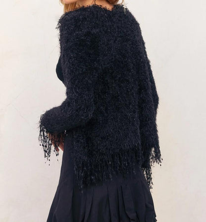 Person in elegant black fringe sweater and skirt against a light background.
