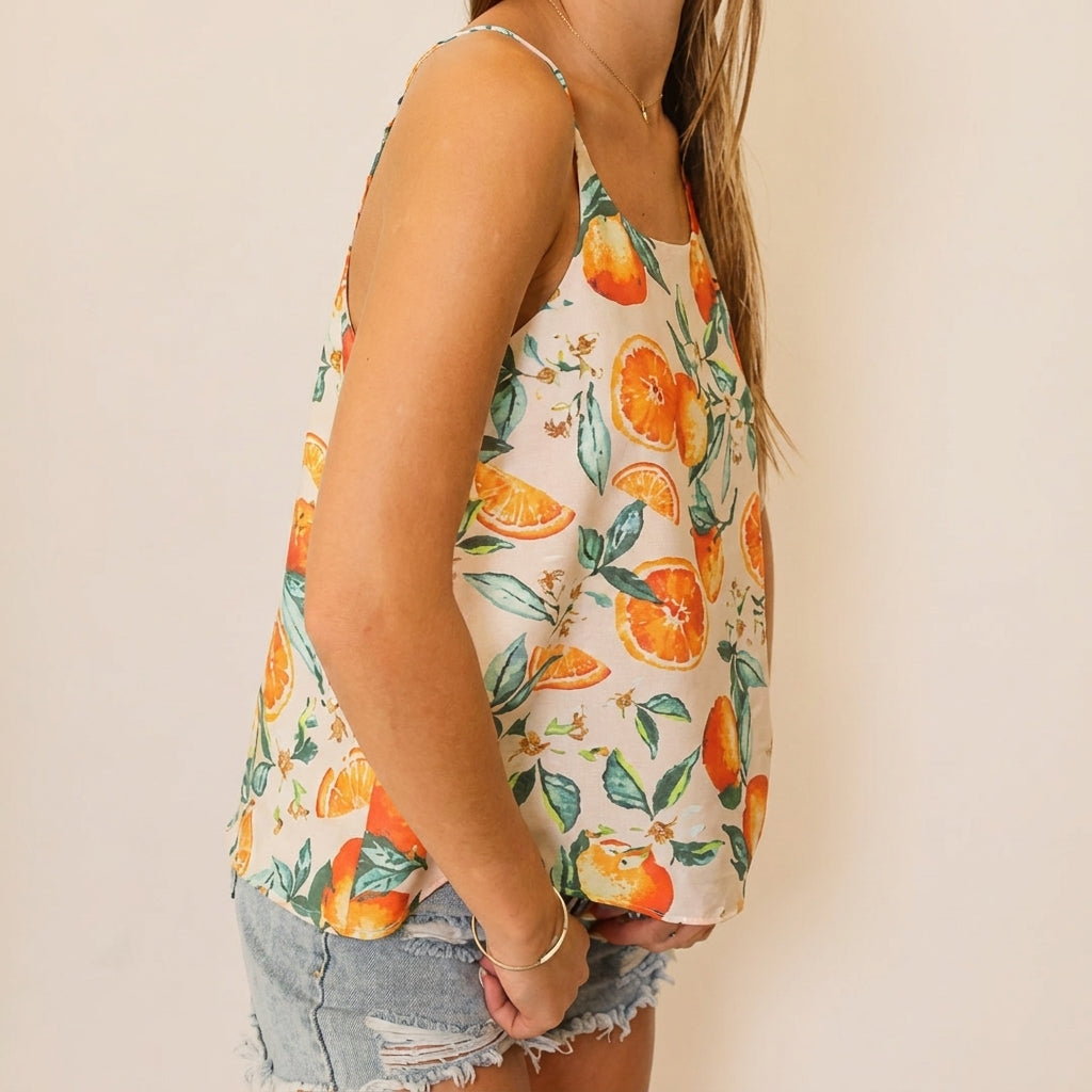 Woman in orange print top and denim shorts, side view.