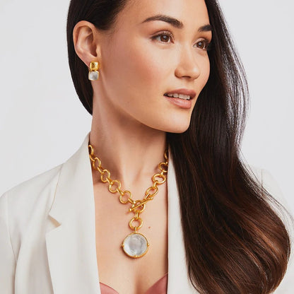Woman wearing gold jewelry and white blazer, looking to the side.
