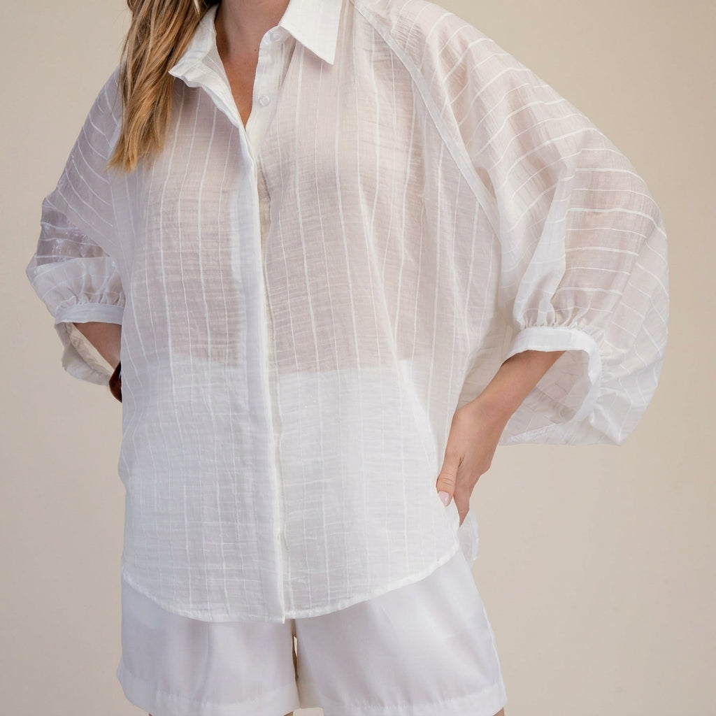 Woman in a sheer white blouse and shorts, hand on hip.