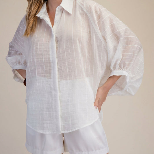 Woman in a sheer white blouse and shorts, hand on hip.