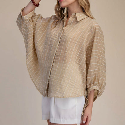 Woman in striped beige blouse and white shorts against a beige background.