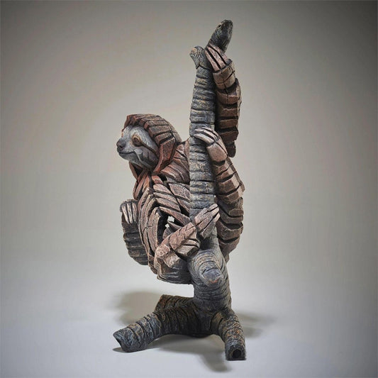 Wooden sculpture of a sloth hanging onto a tree trunk.