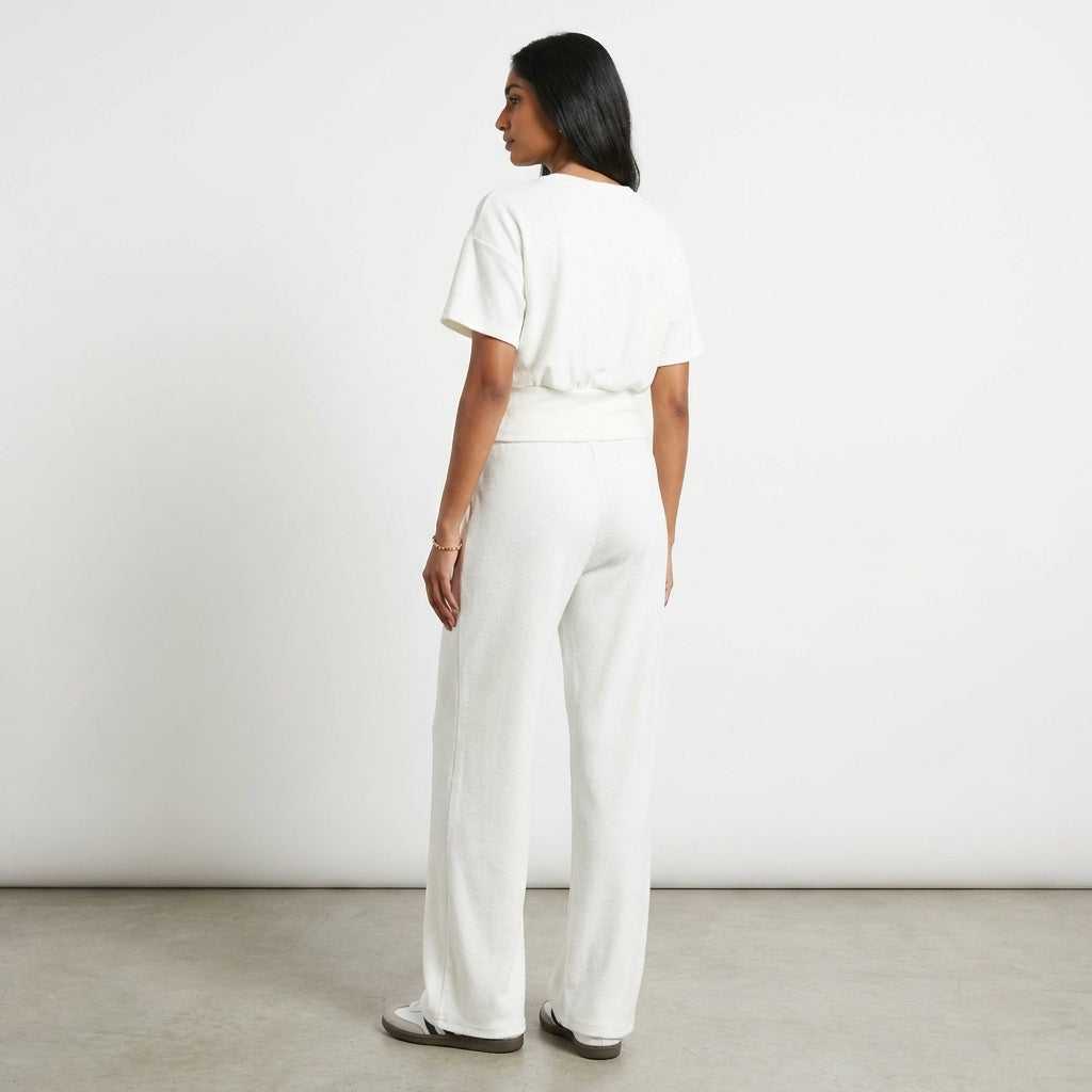 Woman in white outfit standing against a white wall.