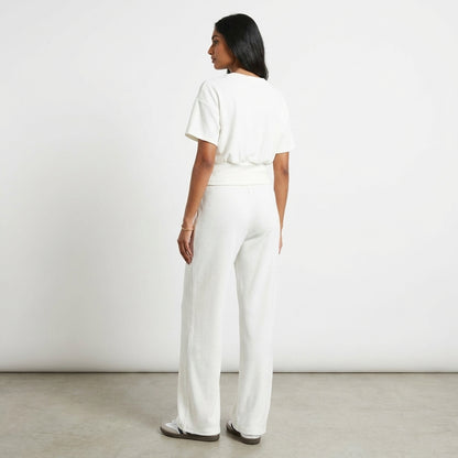 Woman in white outfit standing against a white wall.