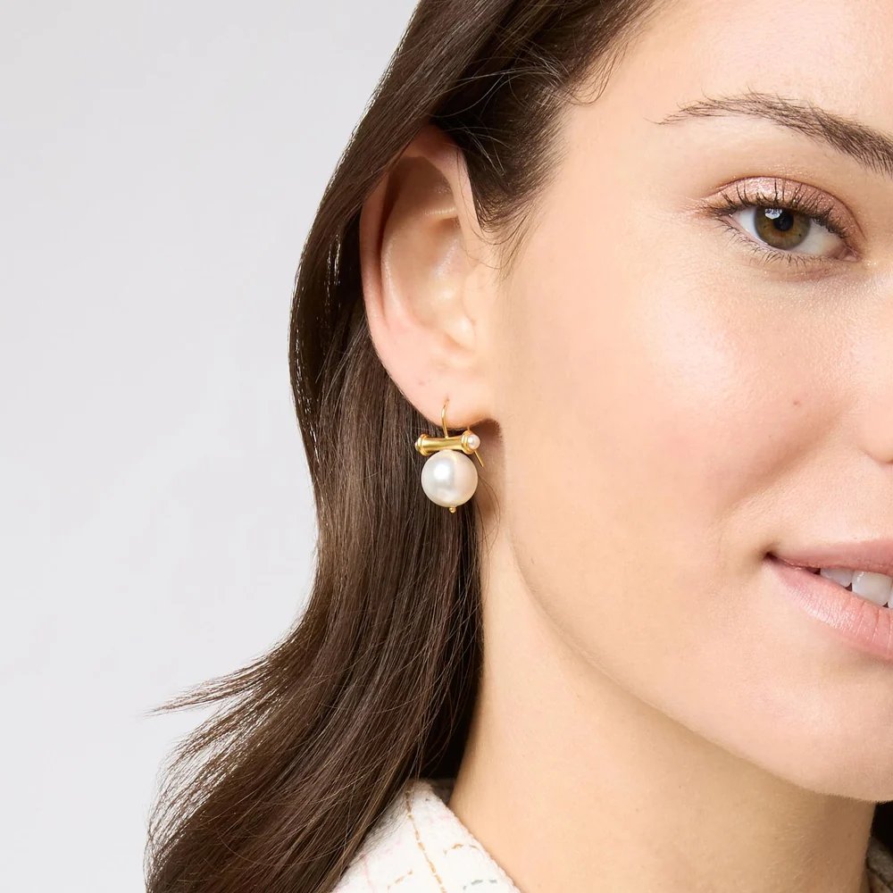 Close-up of a woman wearing a gold earring with a large pearl.