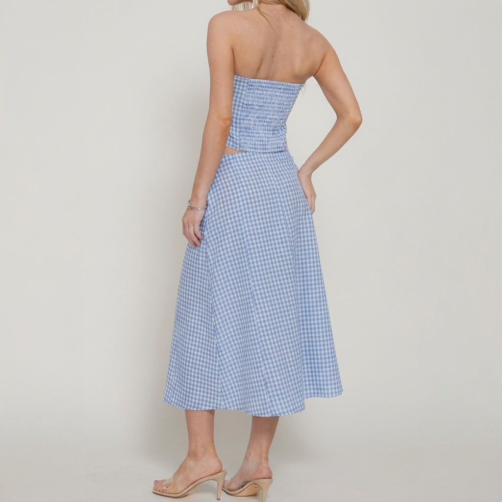 Blonde woman in strapless blue gingham dress, facing away, against white background.