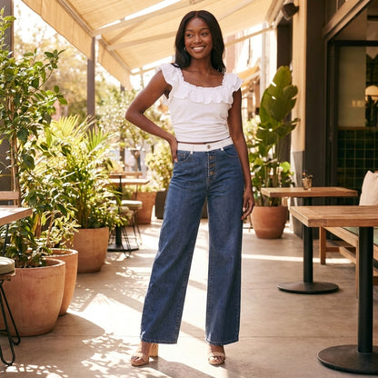 Woman in jeans and white top posing in a sunlit patio with plants.