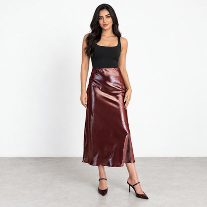 A woman models a black sleeveless top, glossy burgundy midi skirt, and matching heels.
