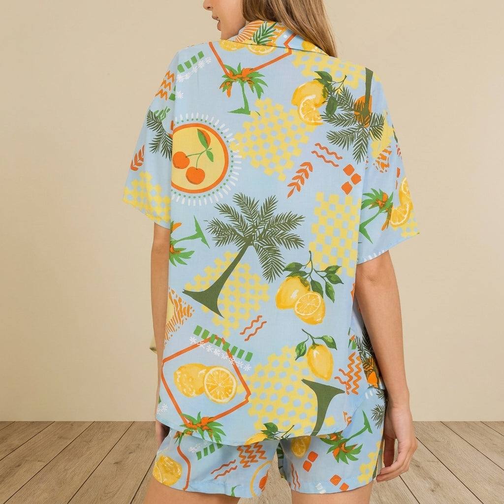 Person in vibrant fruit-patterned shirt with palm trees and lemons on a light blue background.