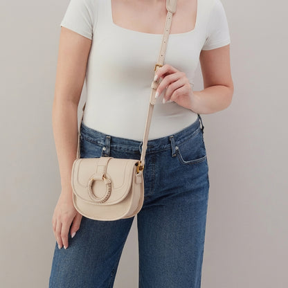 Person holding a beige crossbody bag, wearing jeans and a white top.