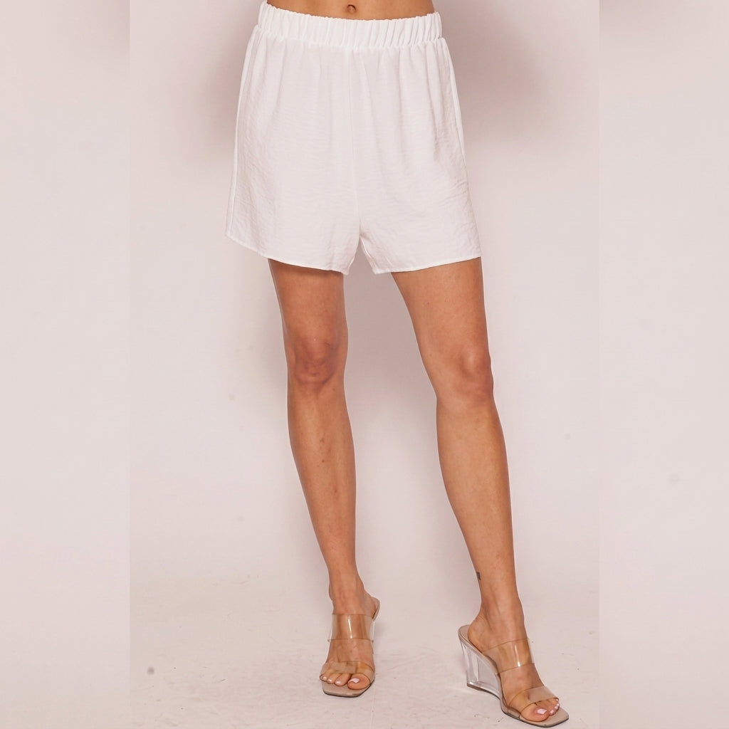 Woman in white shorts and clear heels against a plain background.