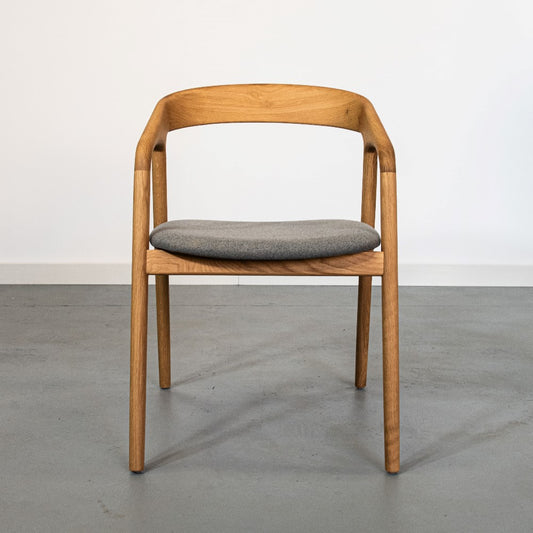 Wooden chair with a curved backrest and gray cushion on a plain floor.