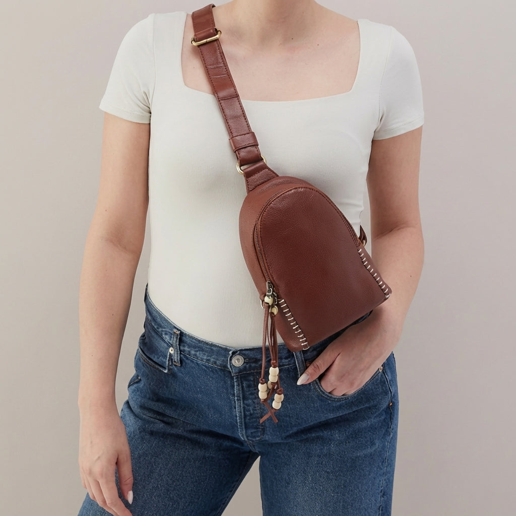 Woman wearing a brown crossbody bag and white top.