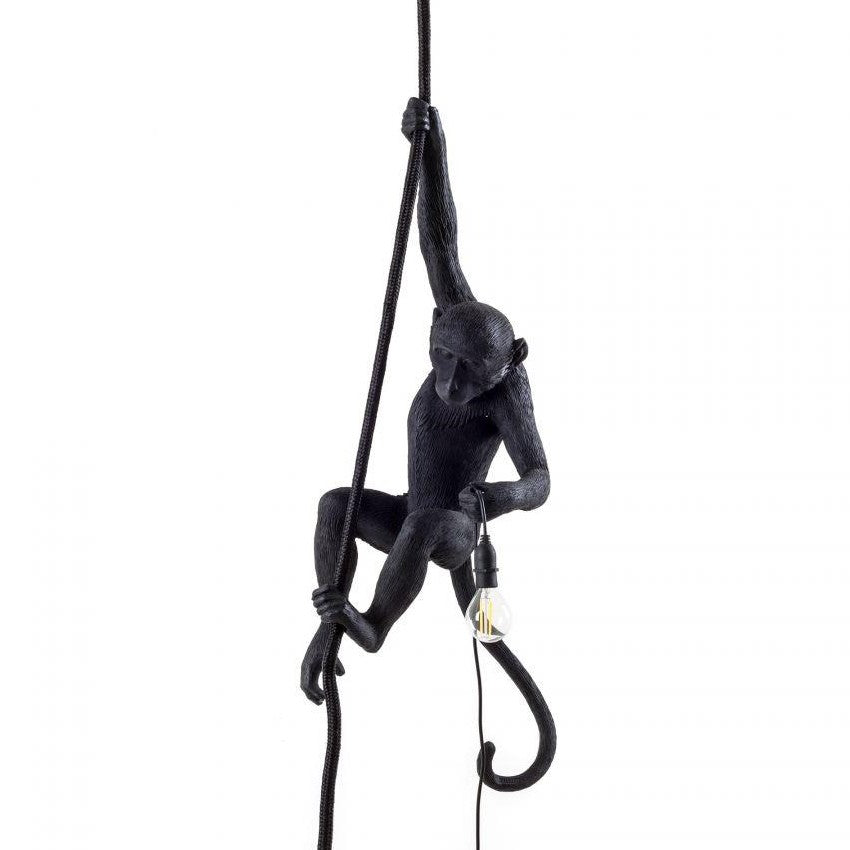 Black monkey lamp holding a light bulb while climbing a rope.