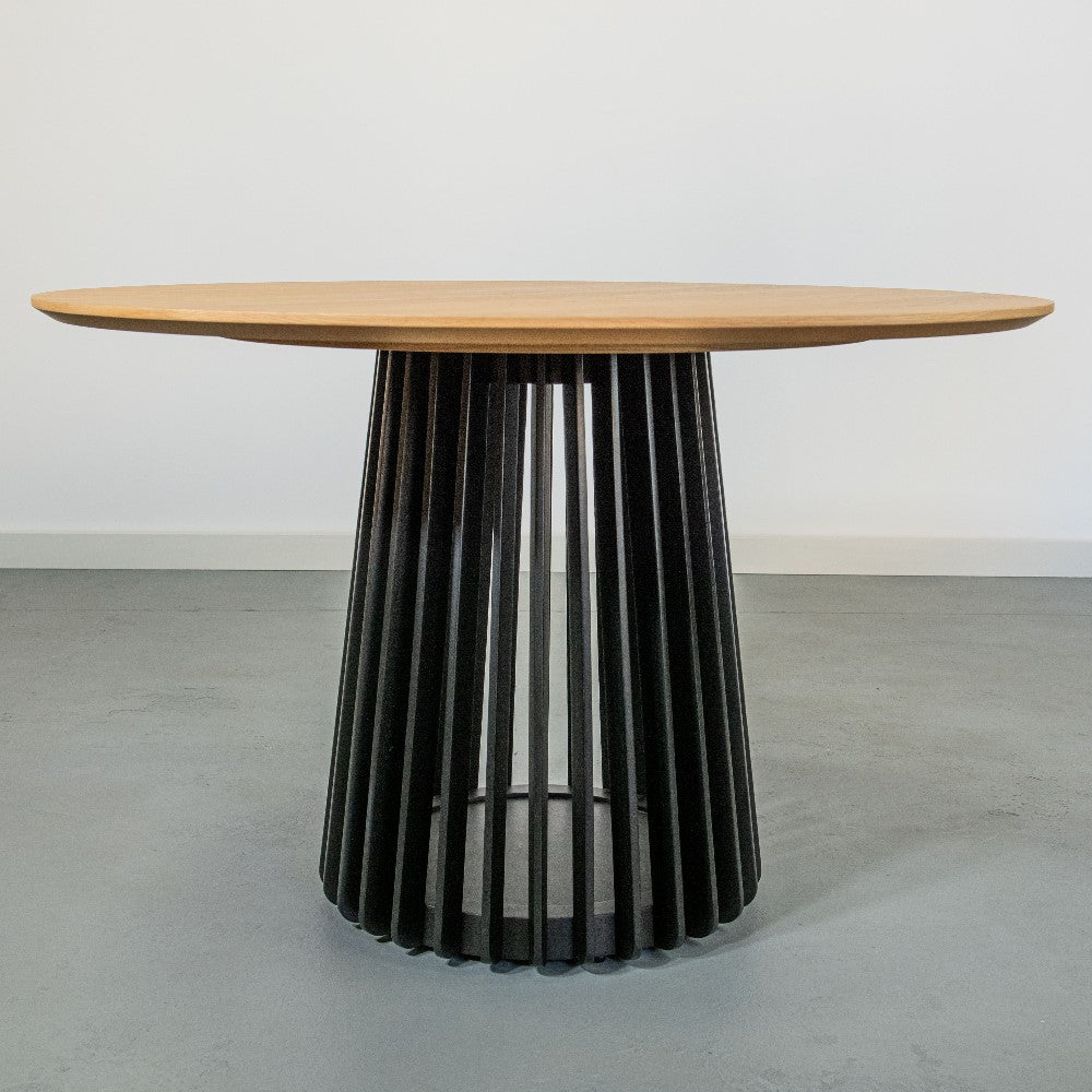 Round wooden table with a slatted black base on a gray floor.