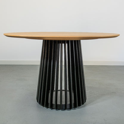 Round wooden table with a slatted black base on a gray floor.