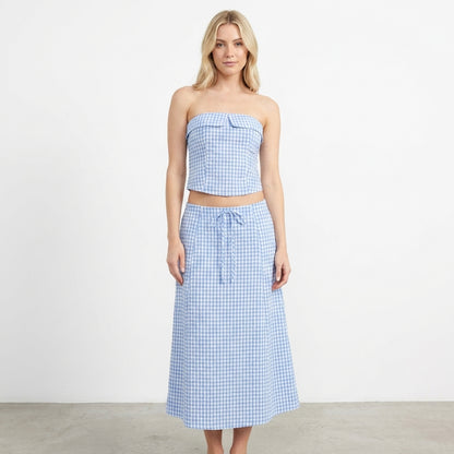Woman in blue gingham strapless top and skirt on white background.