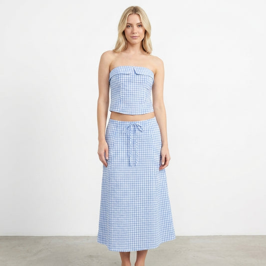 Woman in blue gingham strapless top and skirt on white background.