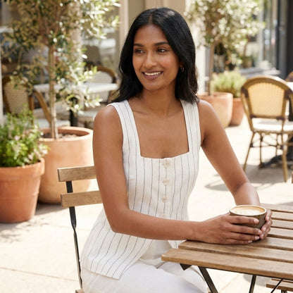 A woman sits outside at a cafe, smiling and holding a coffee.