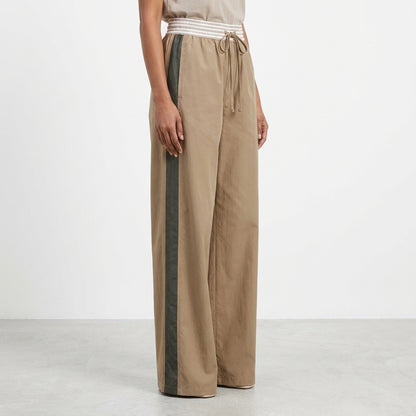 A person wearing loose, tan pants with a green side stripe and a white waistband.