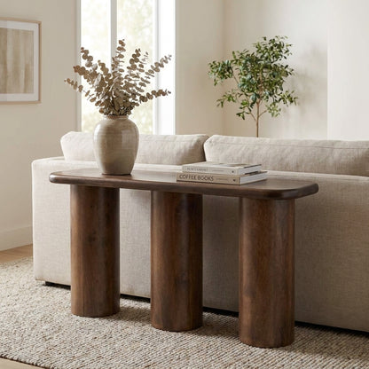 Wooden console table behind sofa with vase and books.