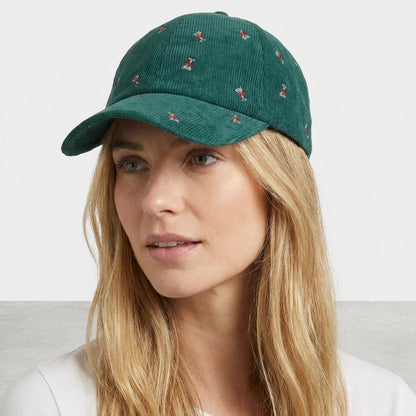 A woman models a green embroidered corduroy cap against a plain studio backdrop.