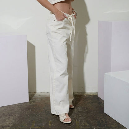 Person in white pants and sandals standing indoors, side view.