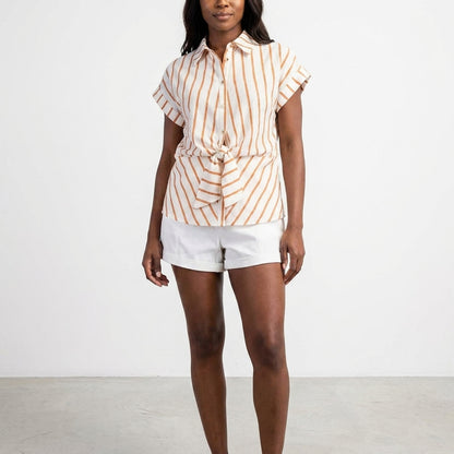Woman in striped shirt and white shorts against plain backdrop.