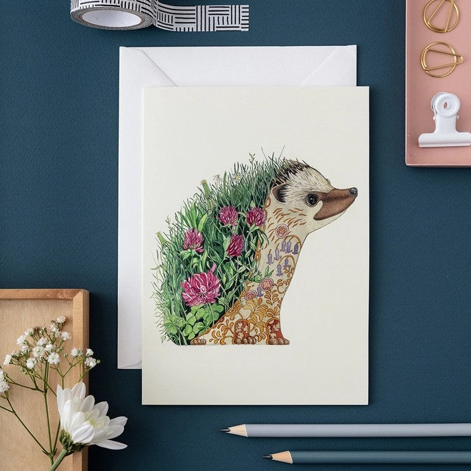 Illustrated hedgehog card with floral design on teal desk.
