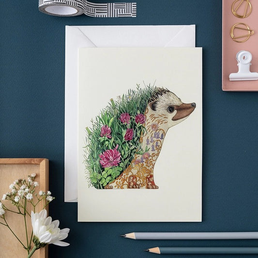 Illustrated hedgehog card with floral design on teal desk.