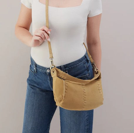 Person holding a tan shoulder bag, wearing a white top and blue jeans.