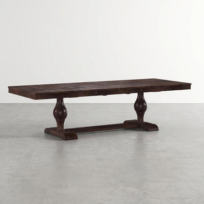 Dark wooden dining table with two pedestal legs on a light gray floor.
