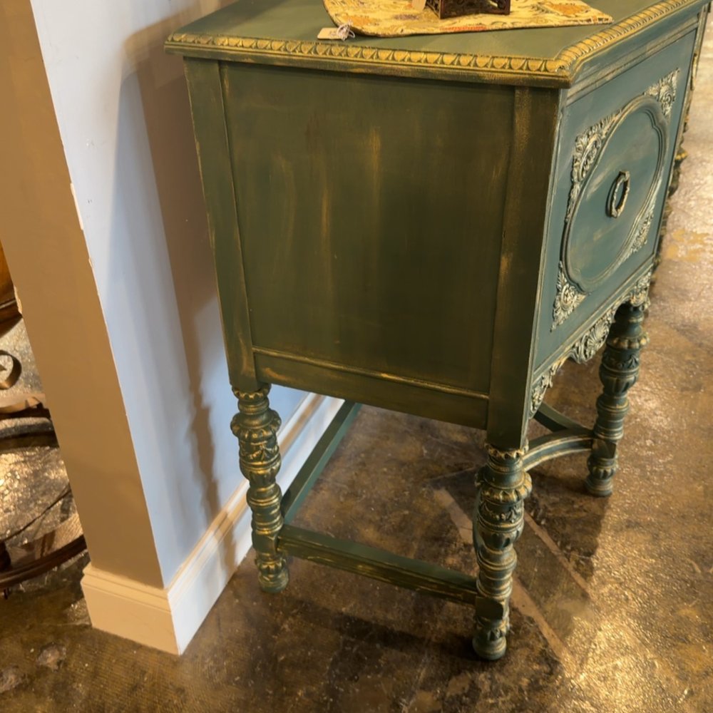 An ornate green wooden cabinet with gilded trim and carved legs stands in a room.