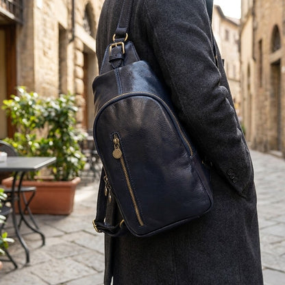 Person in gray coat with navy sling bag in a cobblestone street.